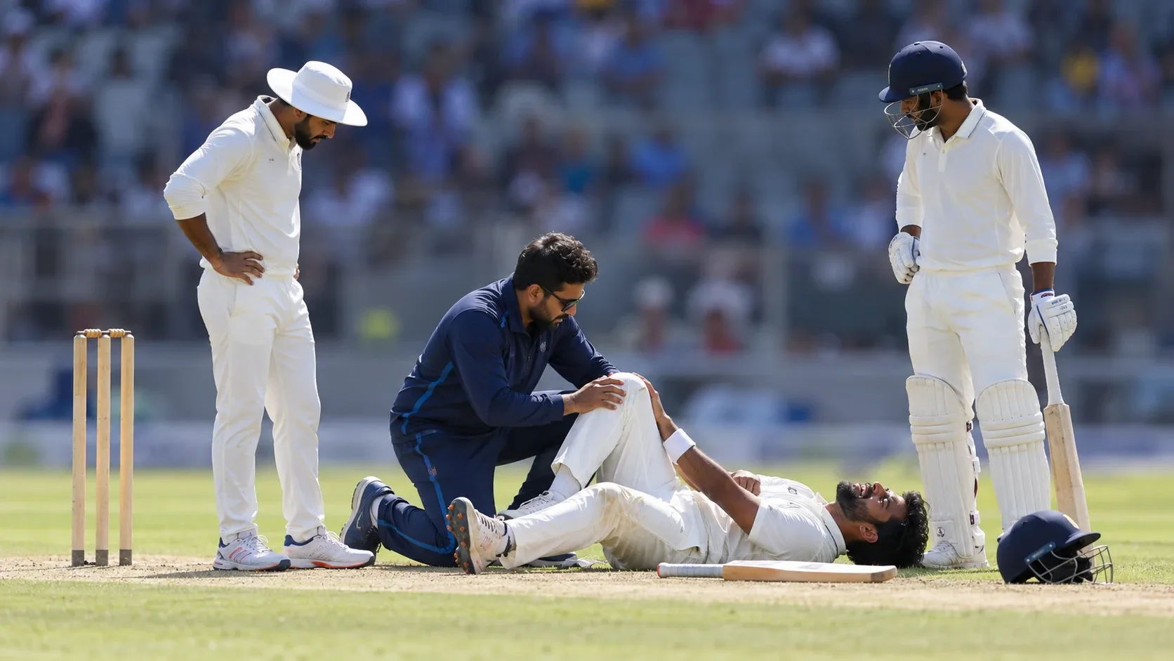 A physiotherapist checking an injured cricketer's knee on the field while teammates look on
